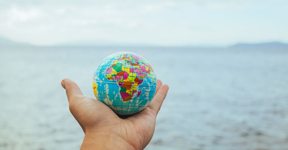 A hand holding a small globe with an ocean backdrop, symbolizing global connection and travel.